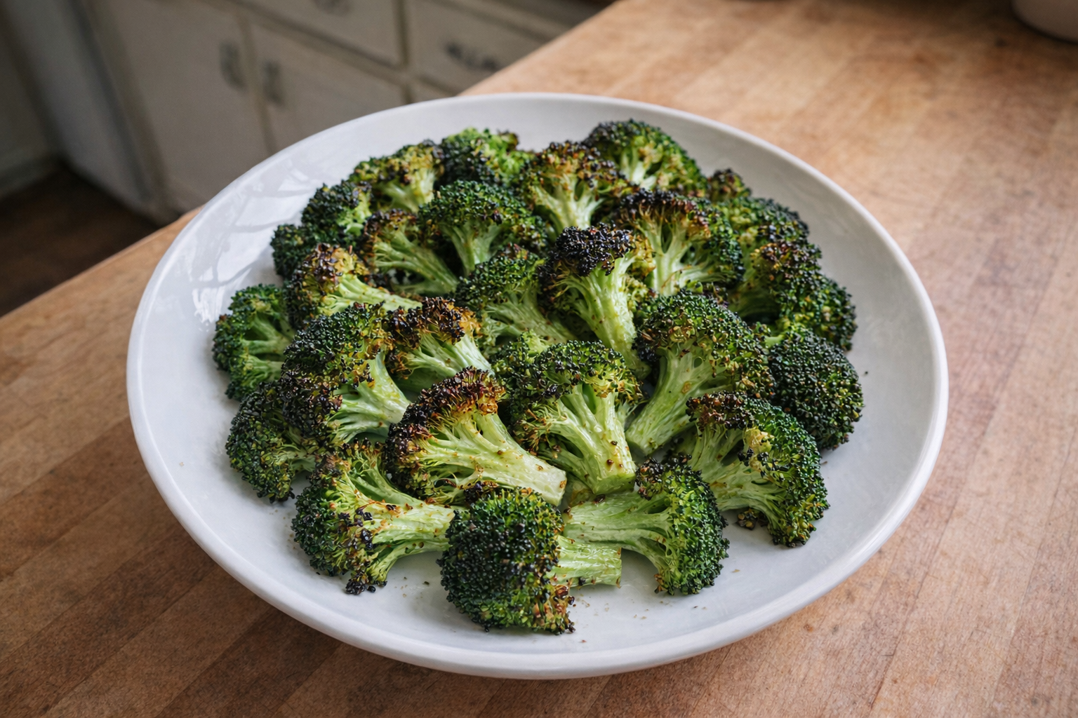 A top-down shot of perfectly roasted broccoli florets arranged on a white plate, showcasing their crispy edges and vibrant green color, natural light